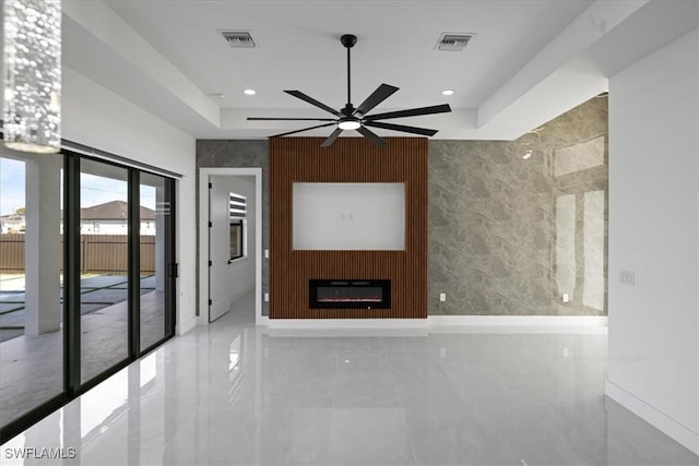 unfurnished living room featuring a tray ceiling, a large fireplace, and ceiling fan