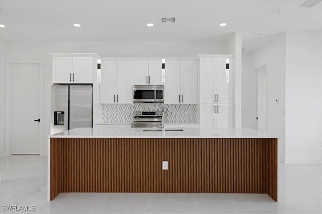 kitchen with sink, appliances with stainless steel finishes, white cabinetry, an island with sink, and decorative backsplash