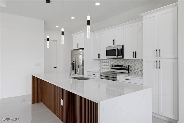 kitchen featuring white cabinetry, a center island with sink, pendant lighting, stainless steel appliances, and backsplash