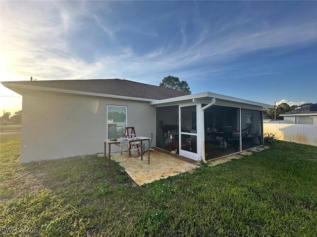 rear view of property featuring a patio, fence, a yard, a sunroom, and stucco siding