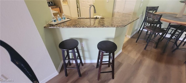 kitchen with baseboards, a kitchen breakfast bar, a sink, and wood finished floors