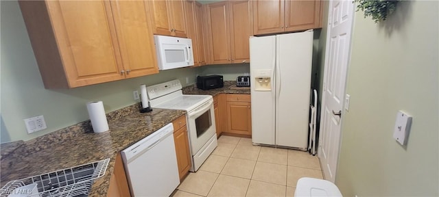 kitchen with light tile patterned floors, white appliances, and dark stone counters