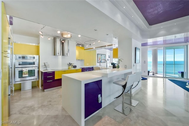 kitchen with a breakfast bar, sink, a water view, stainless steel double oven, and black electric stovetop