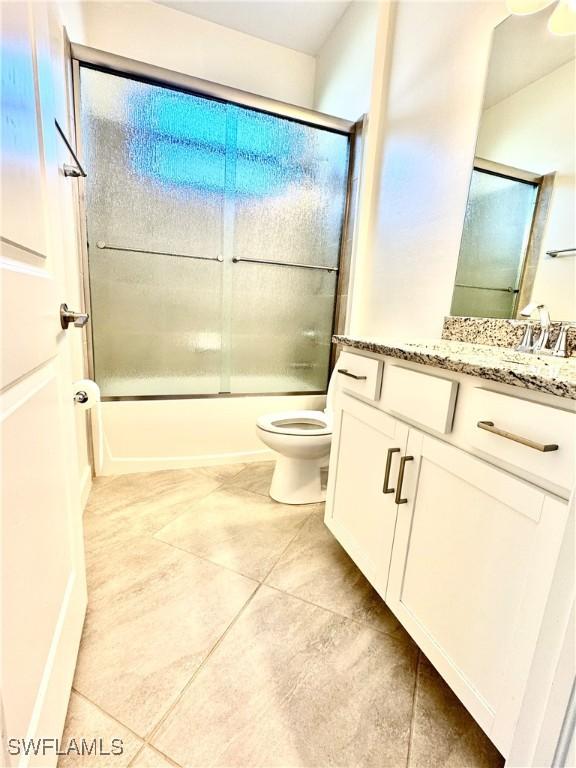 full bathroom featuring toilet, vanity, bath / shower combo with glass door, and tile patterned flooring