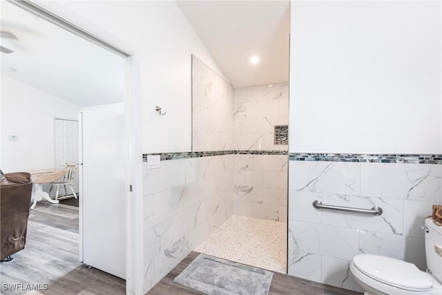 bathroom with tiled shower, lofted ceiling, toilet, tile walls, and hardwood / wood-style flooring