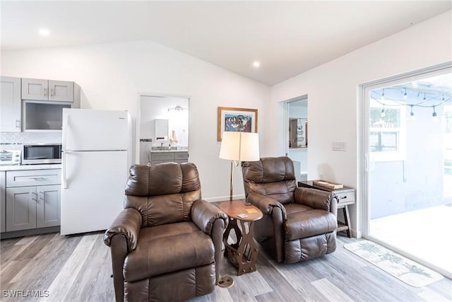 living area with light wood-type flooring, lofted ceiling, and baseboards