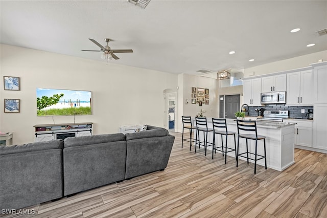 living room featuring ceiling fan, sink, and light hardwood / wood-style floors