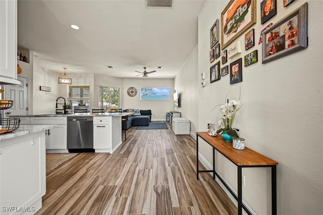 kitchen with white cabinetry, hanging light fixtures, stainless steel dishwasher, and light hardwood / wood-style floors