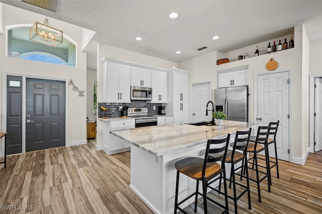 kitchen featuring white cabinetry, stainless steel appliances, a breakfast bar, and a center island with sink