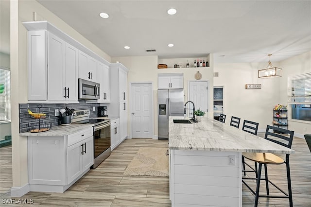 kitchen with stainless steel appliances, a breakfast bar, a kitchen island with sink, and white cabinets