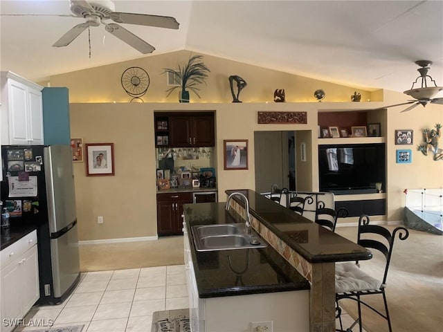 kitchen with sink, a breakfast bar area, stainless steel fridge, a kitchen island with sink, and white cabinets