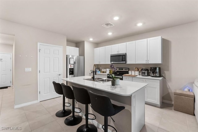 kitchen with sink, appliances with stainless steel finishes, an island with sink, white cabinets, and a kitchen bar