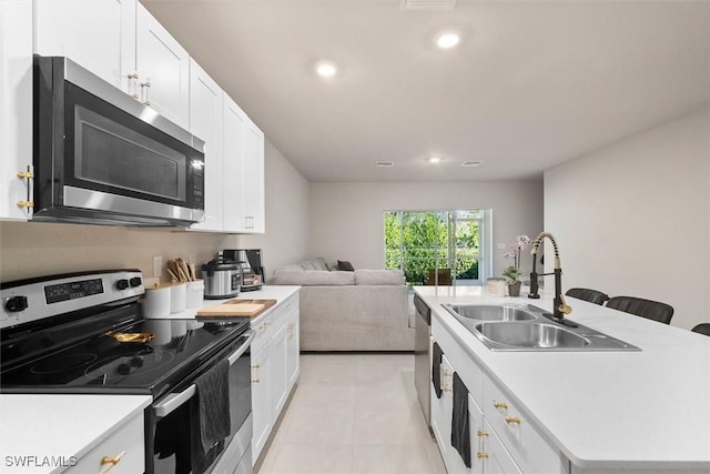 kitchen featuring sink, light tile patterned floors, appliances with stainless steel finishes, white cabinetry, and a center island with sink