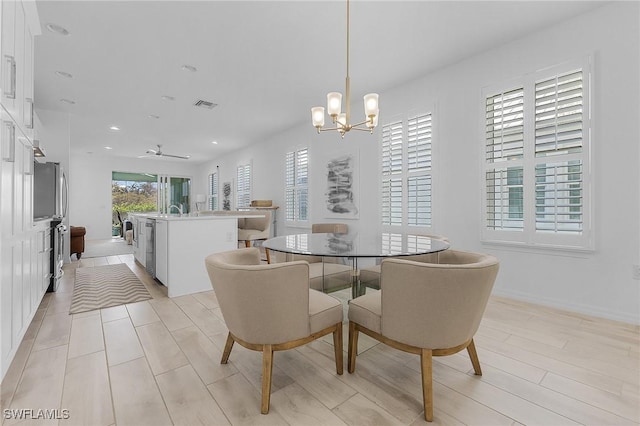 dining space with sink, light hardwood / wood-style floors, and ceiling fan with notable chandelier