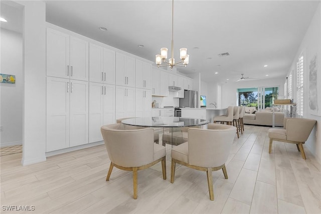 dining room with ceiling fan with notable chandelier and light hardwood / wood-style flooring