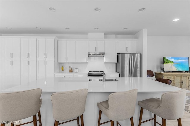 kitchen with appliances with stainless steel finishes, white cabinetry, sink, a kitchen breakfast bar, and a large island with sink