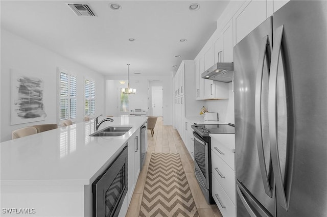 kitchen with sink, decorative light fixtures, a center island with sink, stainless steel appliances, and white cabinets