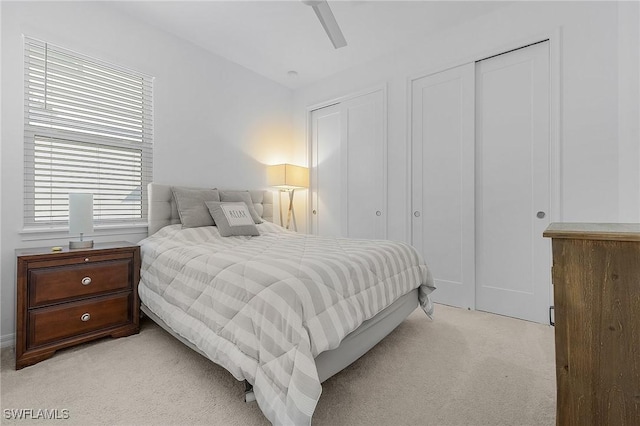 bedroom featuring ceiling fan, light colored carpet, and two closets