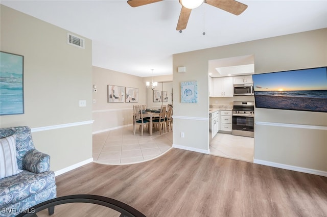 kitchen with white cabinetry, hanging light fixtures, light wood-type flooring, stainless steel appliances, and ceiling fan with notable chandelier