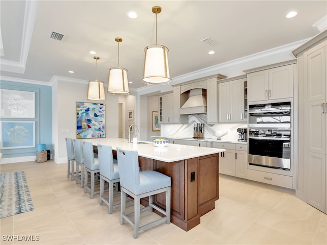 kitchen featuring tasteful backsplash, crown molding, decorative light fixtures, a large island with sink, and custom range hood