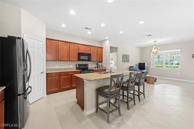 kitchen with a breakfast bar, an island with sink, stainless steel fridge, light stone counters, and electric stove