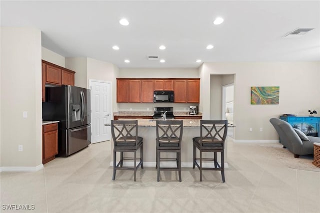 kitchen featuring a breakfast bar, appliances with stainless steel finishes, light stone counters, an island with sink, and light tile patterned flooring