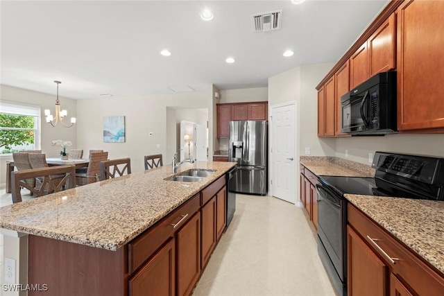 kitchen with light stone countertops, sink, a center island with sink, and black appliances