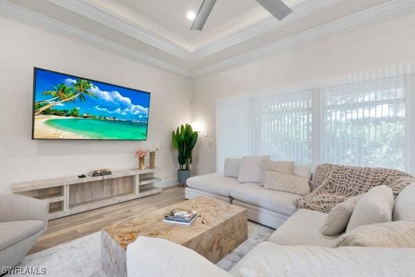 living room featuring crown molding, a raised ceiling, ceiling fan, and light wood-type flooring