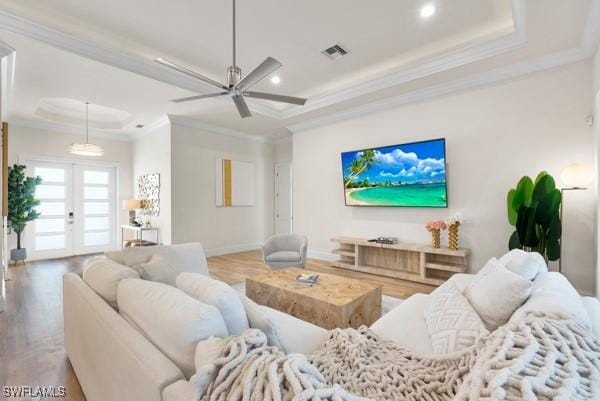 living room with light hardwood / wood-style flooring, ceiling fan, a tray ceiling, ornamental molding, and french doors