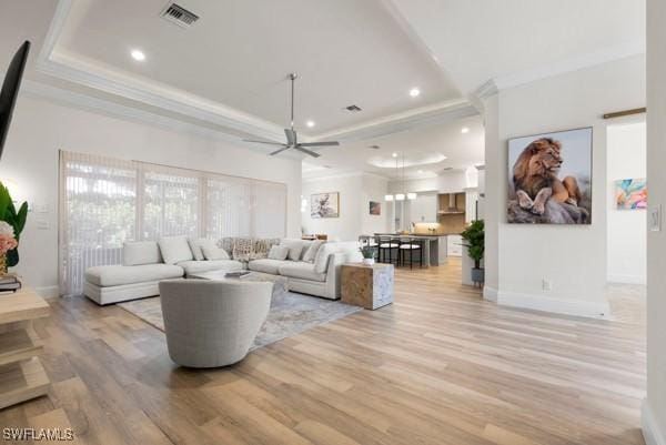 living room with ceiling fan, ornamental molding, a raised ceiling, and light hardwood / wood-style flooring