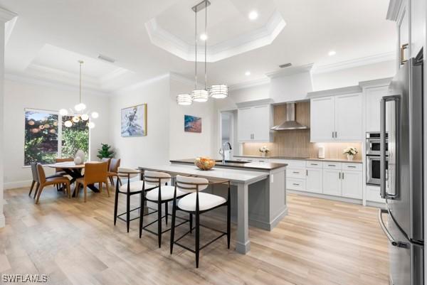 kitchen with wall chimney range hood, a tray ceiling, and hanging light fixtures