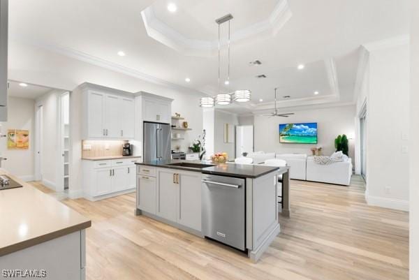 kitchen with appliances with stainless steel finishes, a raised ceiling, and a kitchen island with sink