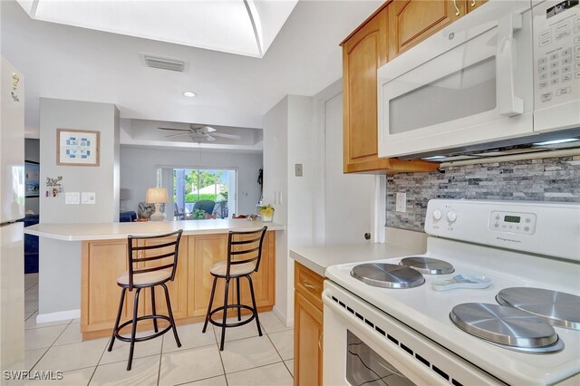 kitchen featuring a breakfast bar, decorative backsplash, ceiling fan, kitchen peninsula, and white appliances