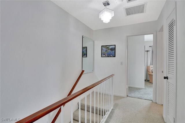 hallway with an upstairs landing, light colored carpet, visible vents, and baseboards