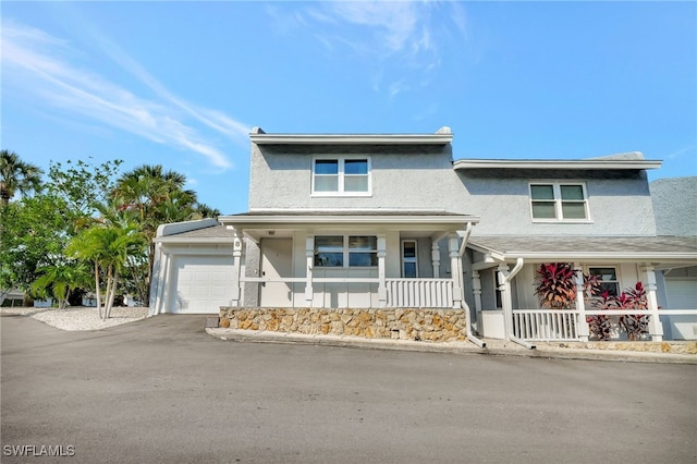 view of front facade with stucco siding, an attached garage, a porch, and driveway