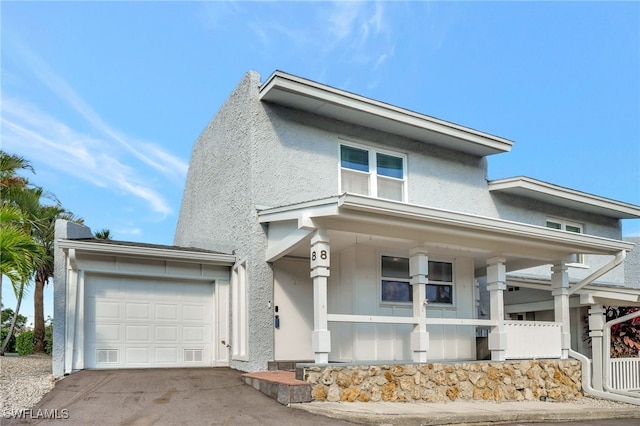 view of front facade featuring covered porch, stucco siding, an attached garage, and driveway