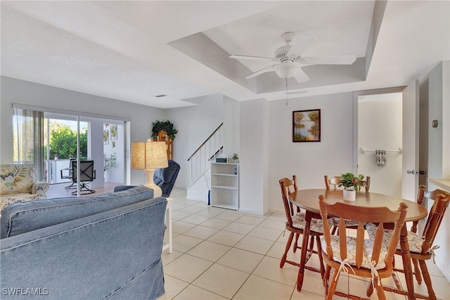 dining space with a ceiling fan, stairway, baseboards, light tile patterned floors, and a raised ceiling