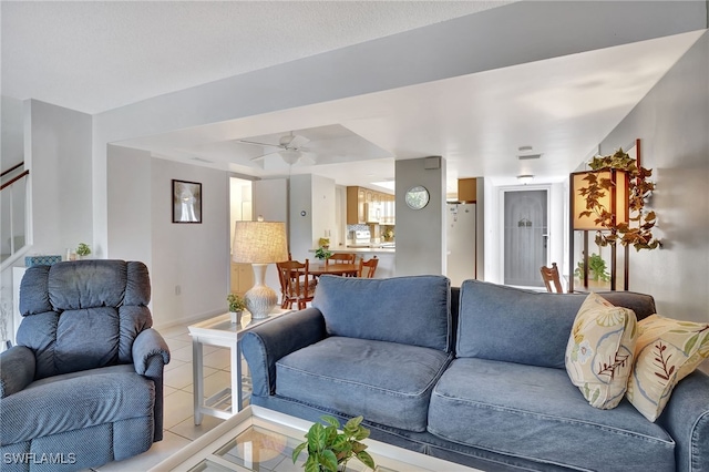 living area featuring light tile patterned floors, baseboards, a ceiling fan, and stairs