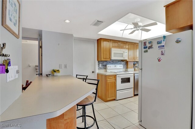 kitchen with a breakfast bar area, white appliances, kitchen peninsula, ceiling fan, and backsplash