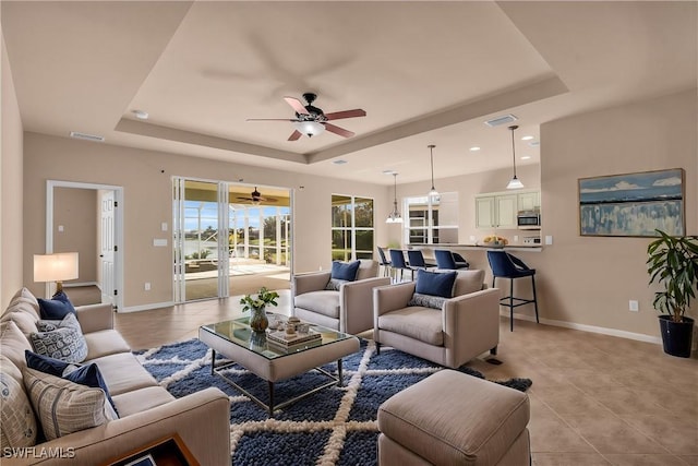 tiled living room with a tray ceiling and ceiling fan