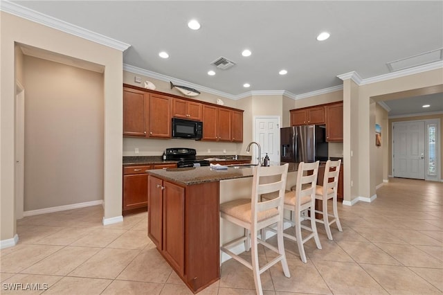 kitchen featuring a kitchen bar, light tile patterned floors, a center island with sink, and black appliances