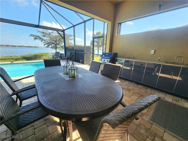 view of patio with a water view, grilling area, sink, and glass enclosure