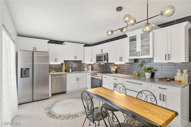 kitchen featuring appliances with stainless steel finishes, decorative light fixtures, sink, white cabinets, and backsplash