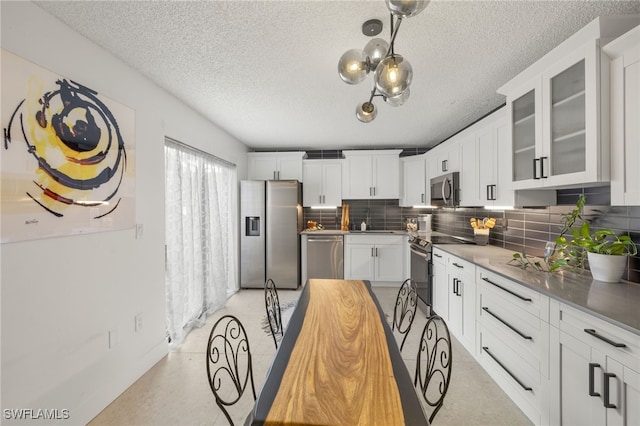 kitchen featuring appliances with stainless steel finishes, decorative light fixtures, white cabinets, decorative backsplash, and a textured ceiling