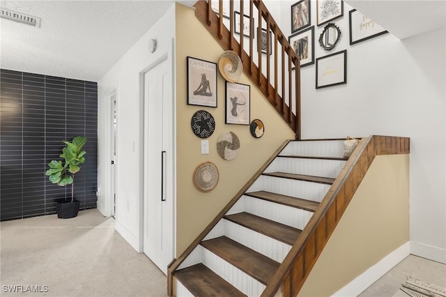 staircase with a textured ceiling and tile walls