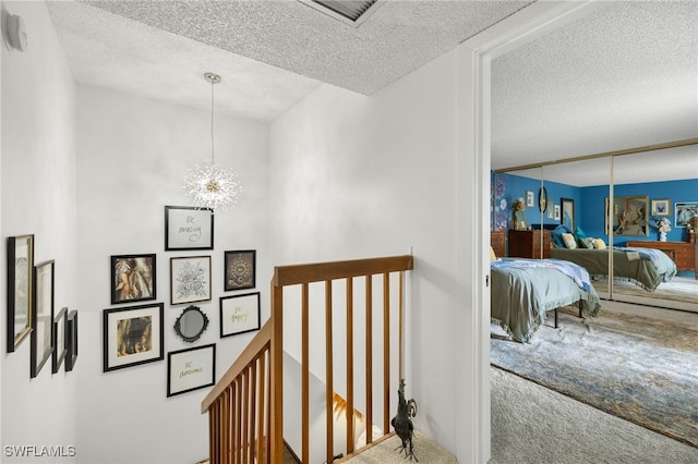 staircase featuring a notable chandelier, carpet, and a textured ceiling