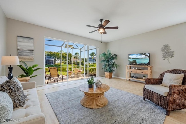 living area with baseboards, light wood-style flooring, a sunroom, and a ceiling fan