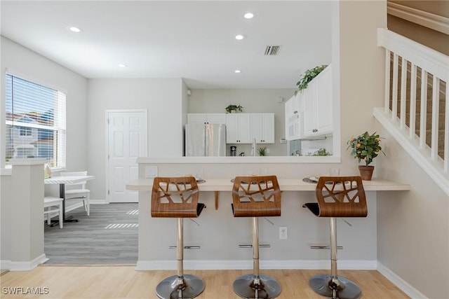 kitchen with white cabinetry, a kitchen breakfast bar, light countertops, light wood-type flooring, and freestanding refrigerator