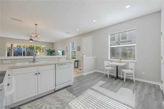 kitchen featuring white appliances, white cabinets, decorative light fixtures, light countertops, and a sink