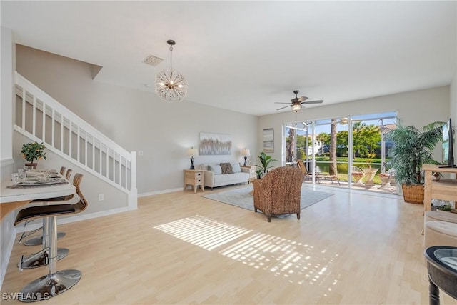 living room featuring baseboards, visible vents, stairs, light wood-type flooring, and ceiling fan with notable chandelier